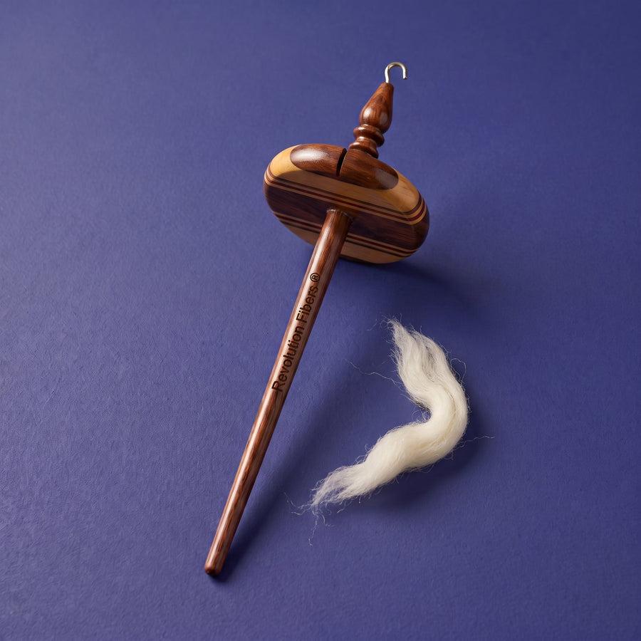 Wooden top-whorl drop spindle with Revolution Fibers branding and ivory wool fiber on an indigo background.