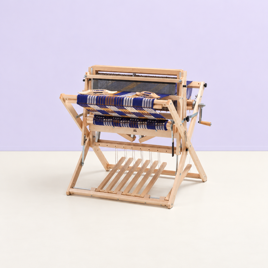 Schacht Baby Wolf floor loom with indigo, ivory, and ochre woven cloth in a bright studio with a pale lavender wall.