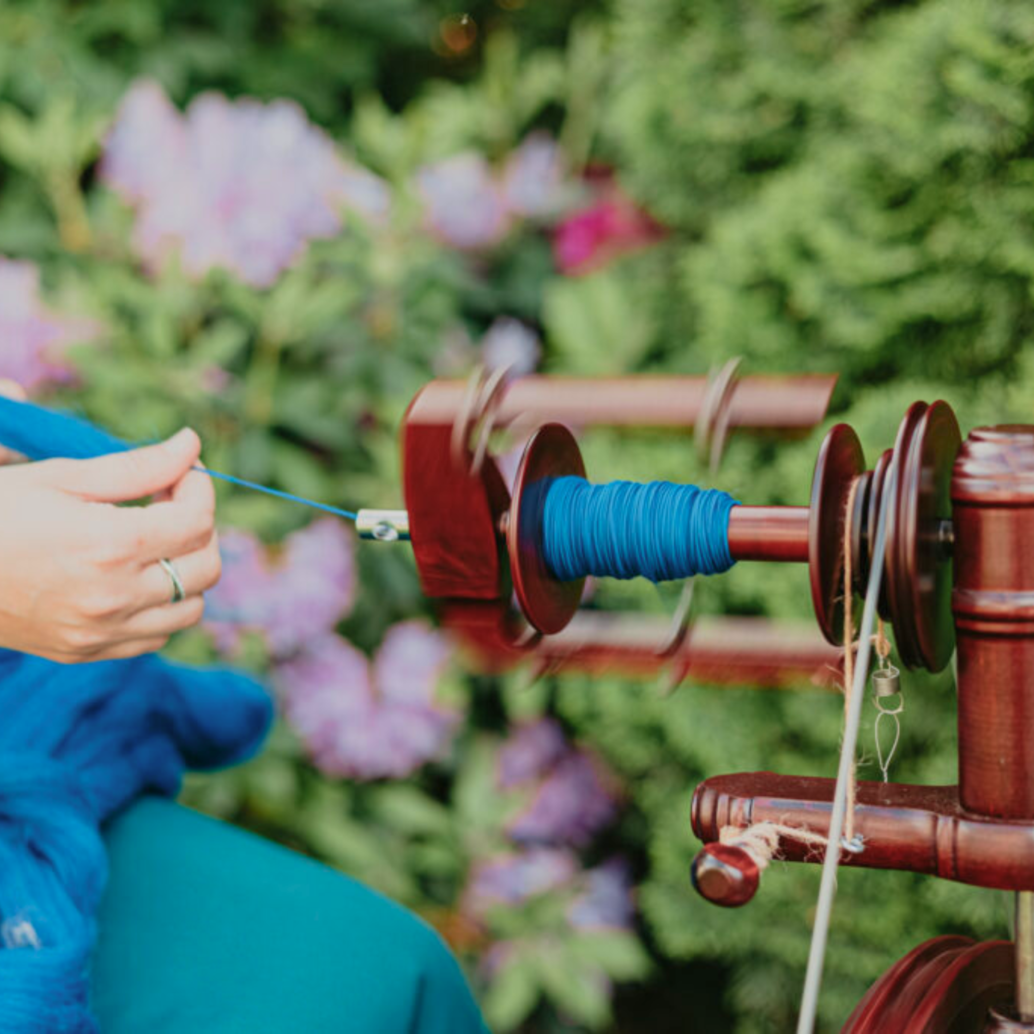 Outdoor spinning moment: Kromski Sonata Encore bobbin with blue yarn in a garden setting, highlighting portable handspinning.