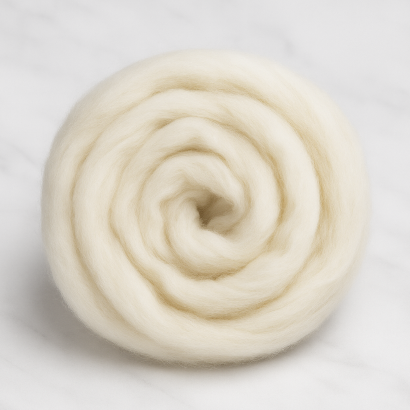 Rambouillet combed top coiled into a flat spiral on marble, undyed ecru color.