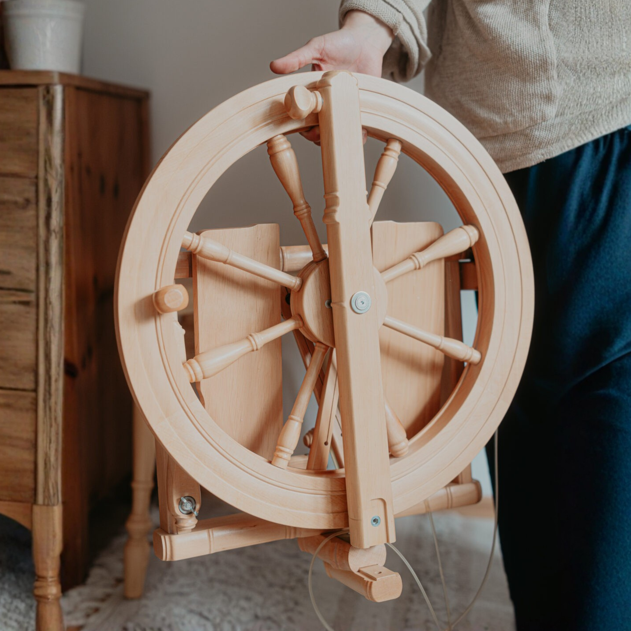 Person holding folded Kromski Sonata Encore spinning wheel indoors, showing how the travel wheel carries like a compact case.