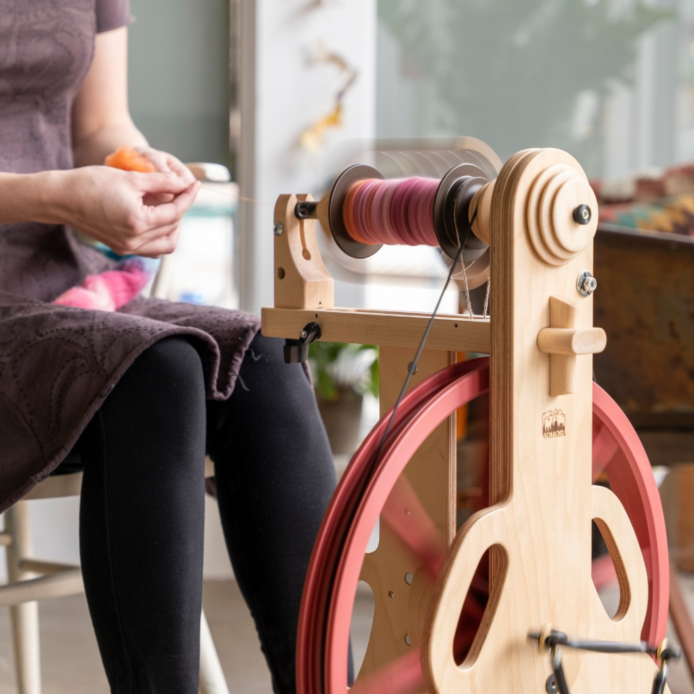 Lifestyle close-up of a spinner drafting fiber on the Schacht Ladybug Classic Maple with the red drive wheel.