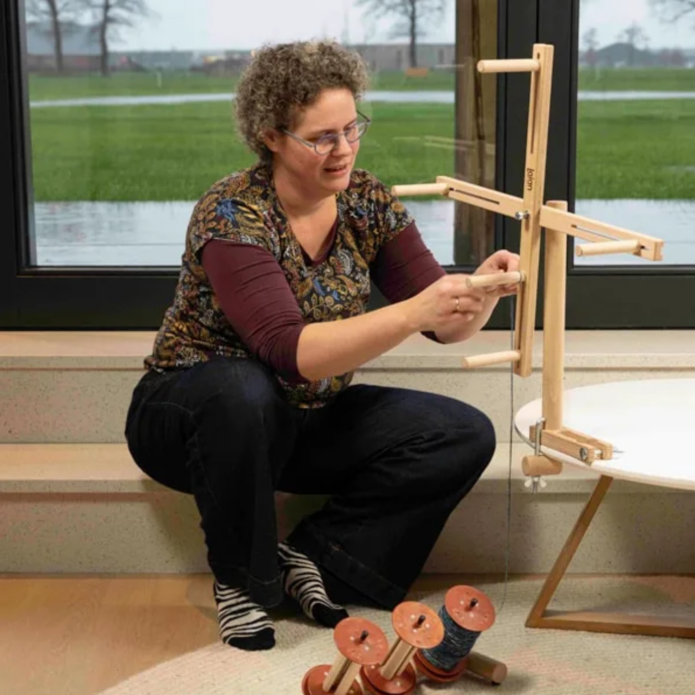 Spinner winding yarn on Lojan Skeinwinder attached to table — adjustable skein size