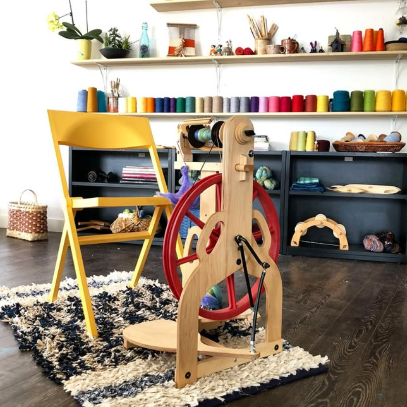 Home craft-room scene featuring the Schacht Ladybug Classic Maple spinning wheel with red drive wheel beside shelving and supplies.