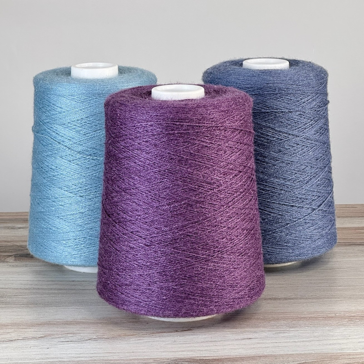 Trio of elderberry, sky, and slate cones arranged upright on a tabletop; 1 lb. cones, 2/18 lace, 4455 yards—silky blend for warp or weft.