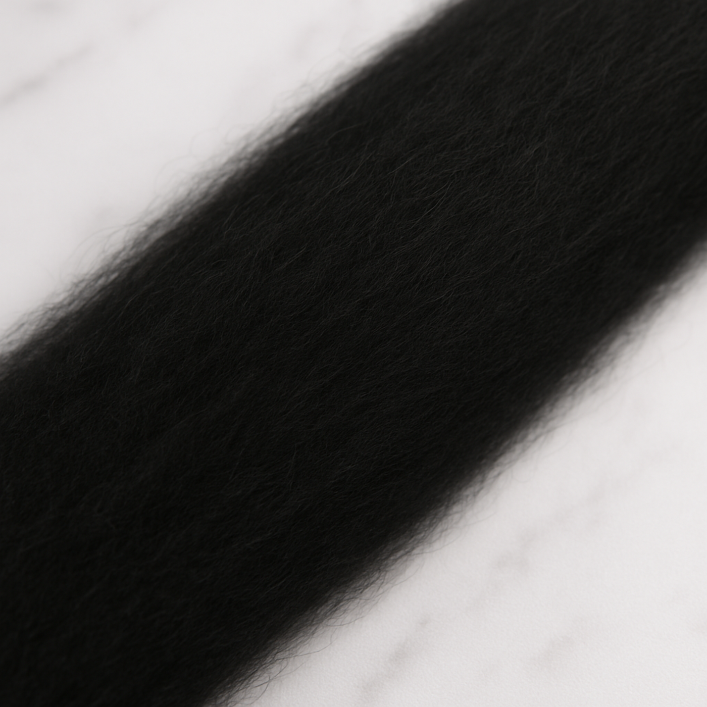 Extreme close-up of black 19-micron Merino carded sliver on marble—matte, evenly carded loft ideal for felting or drafting to spin.