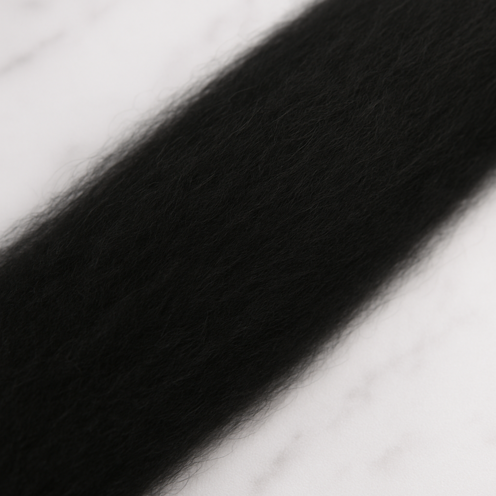 Extreme close-up of black 19-micron Merino carded sliver on marble—matte, evenly carded loft ideal for felting or drafting to spin.
