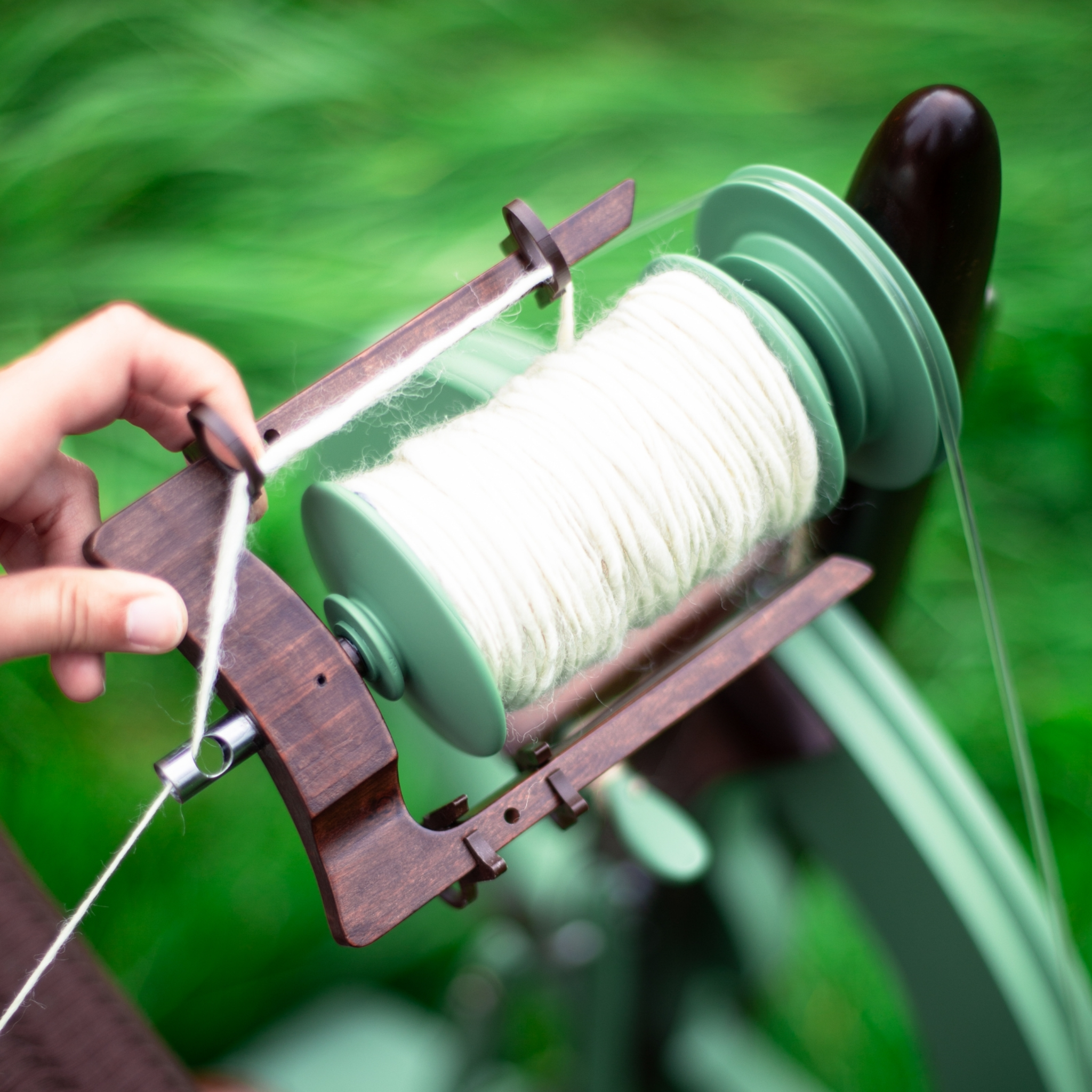 Macro shot of the bobbin mechanism on the limited edition Kromski Fantasia in meadow green with walnut accents. Placed outdoors in a meadow setting.