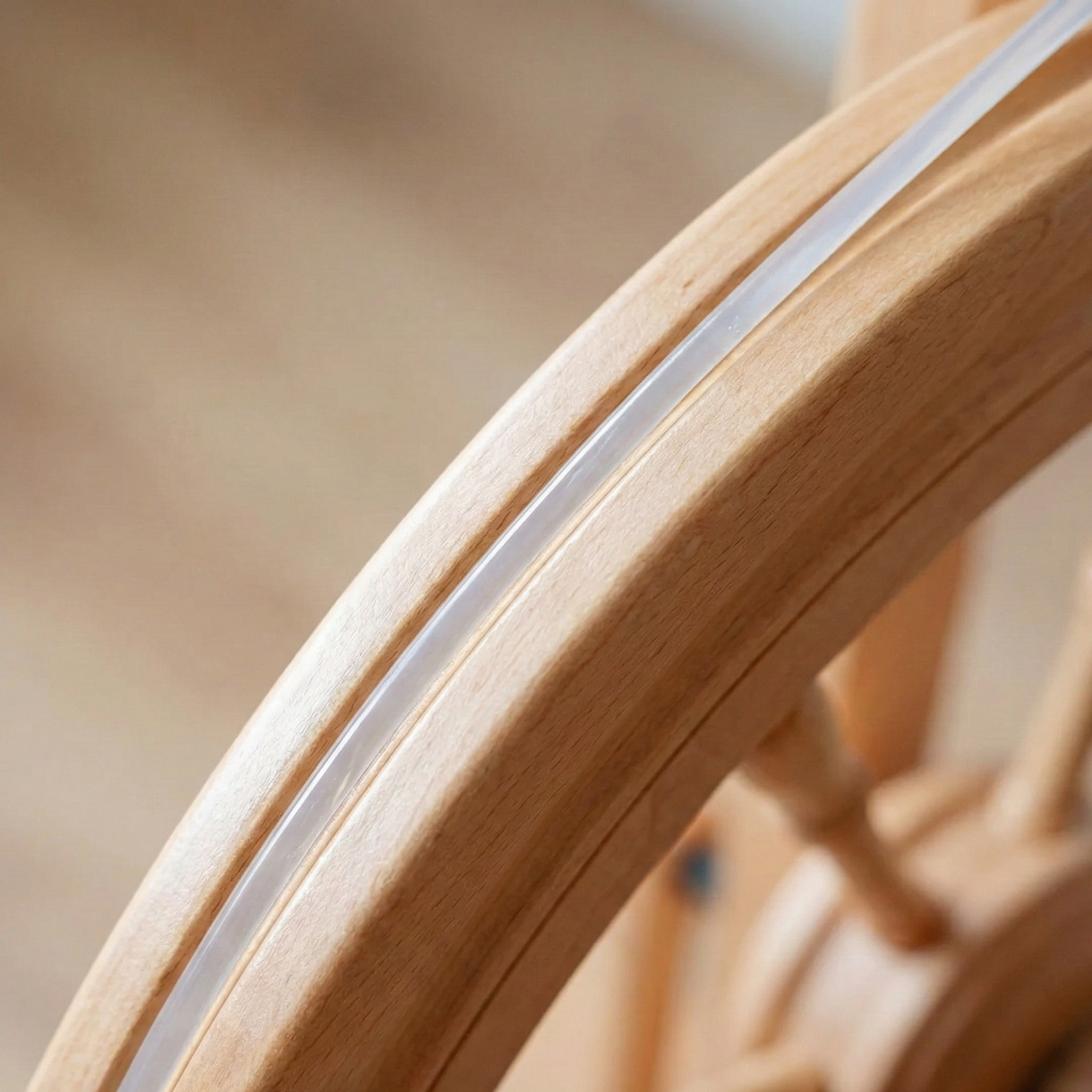 Close-up of a Kromski poly drive band seated in the drive wheel groove on a wooden spinning wheel, Revolution Fibers.