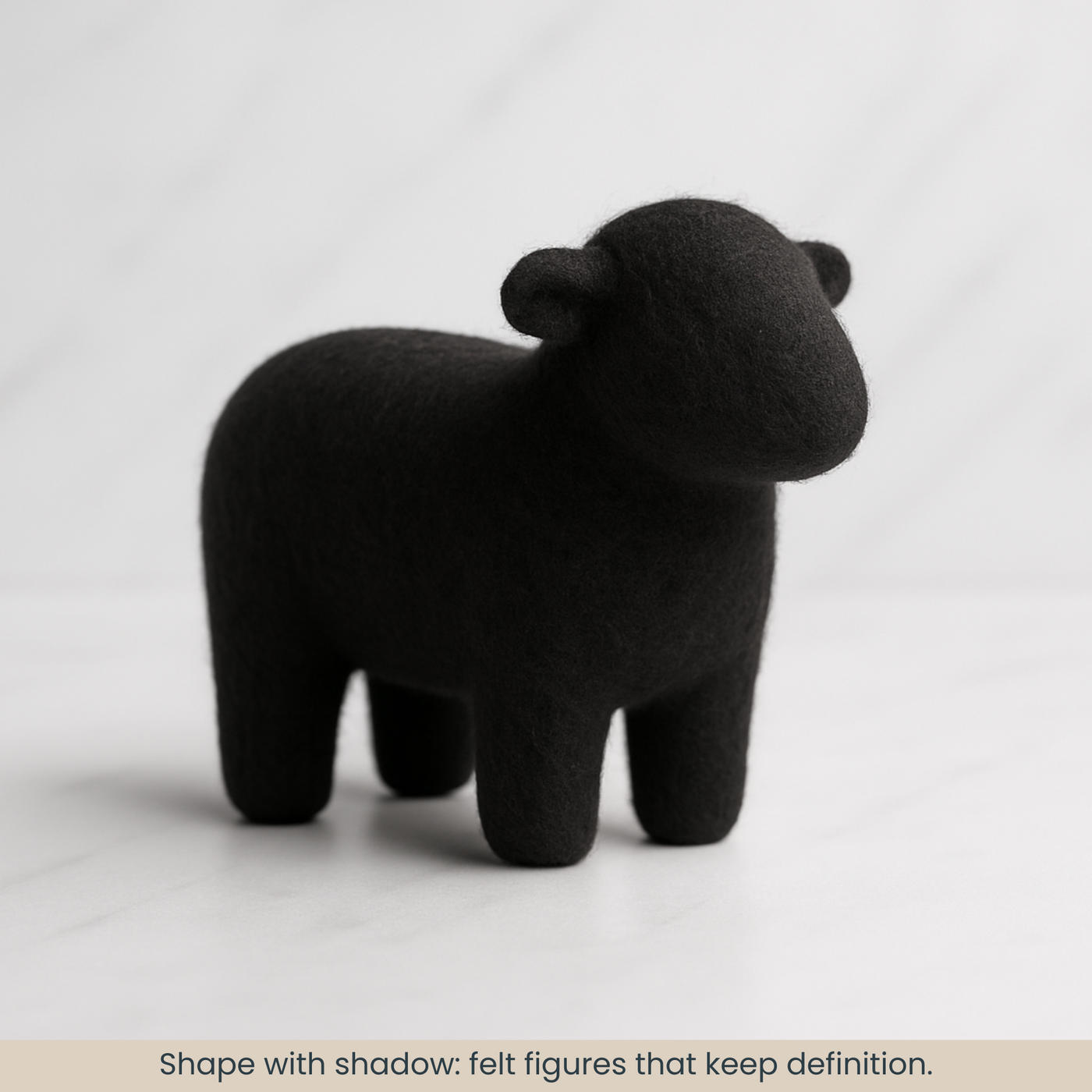 Needle-felted sheep made from black 19-micron Merino carded sliver, smooth matte finish with a defined silhouette on a white marble backdrop.