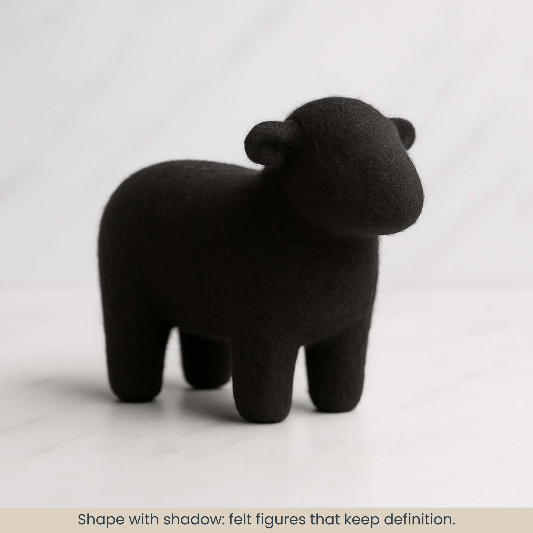 Needle-felted sheep made from black 19-micron Merino carded sliver, smooth matte finish with a defined silhouette on a white marble backdrop.