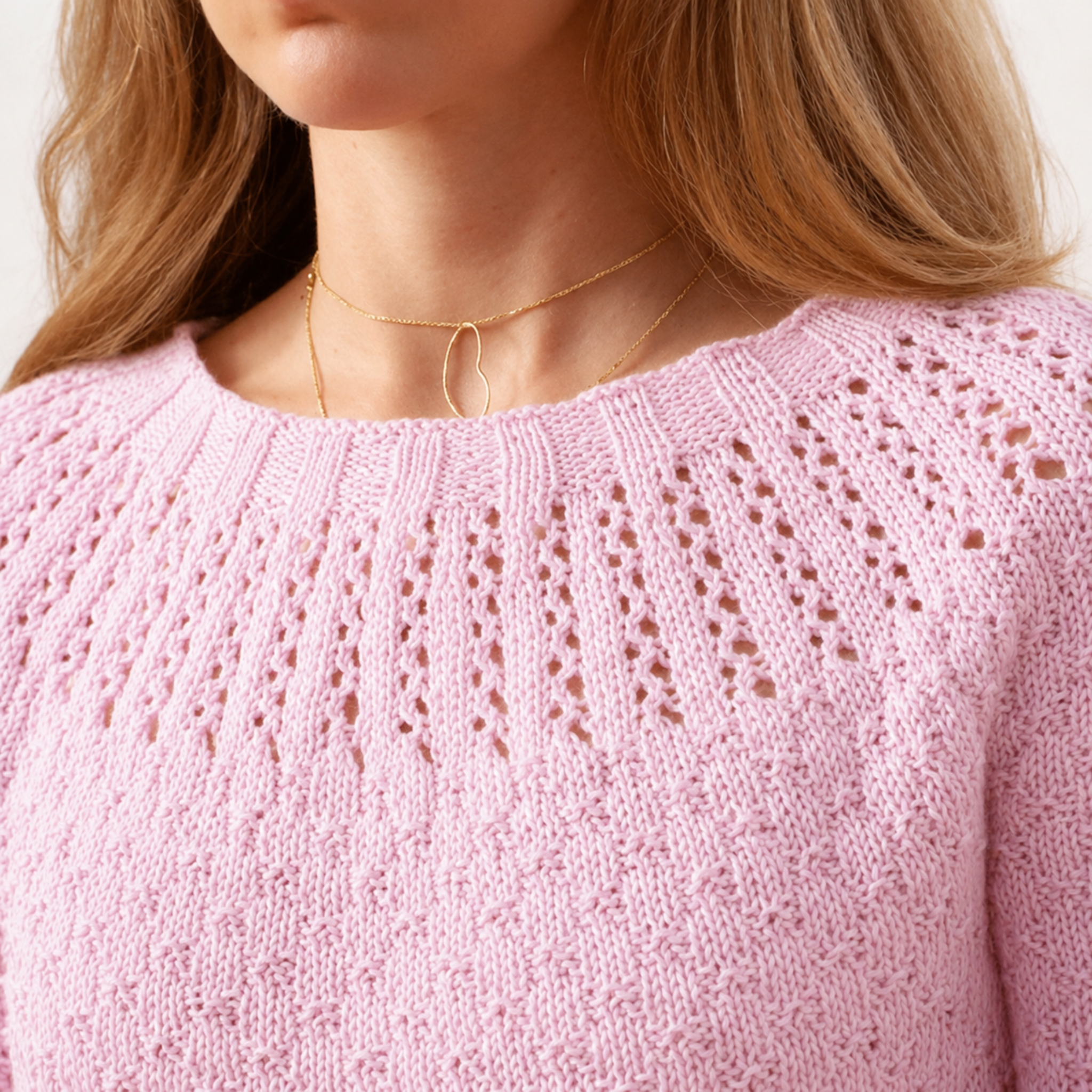 Close-up of the Arnavut Textured Tee knitting pattern showing the eyelet yoke and textured stitches in soft pink Cotton Fleece DK yarn.