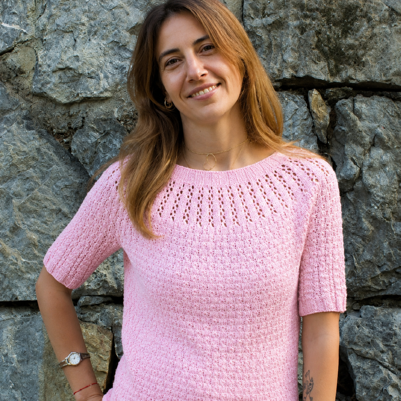 Arnavut Textured Tee knitting pattern shown on a model in a solid pink cotton-blend DK yarn with textured body and eyelet yoke.