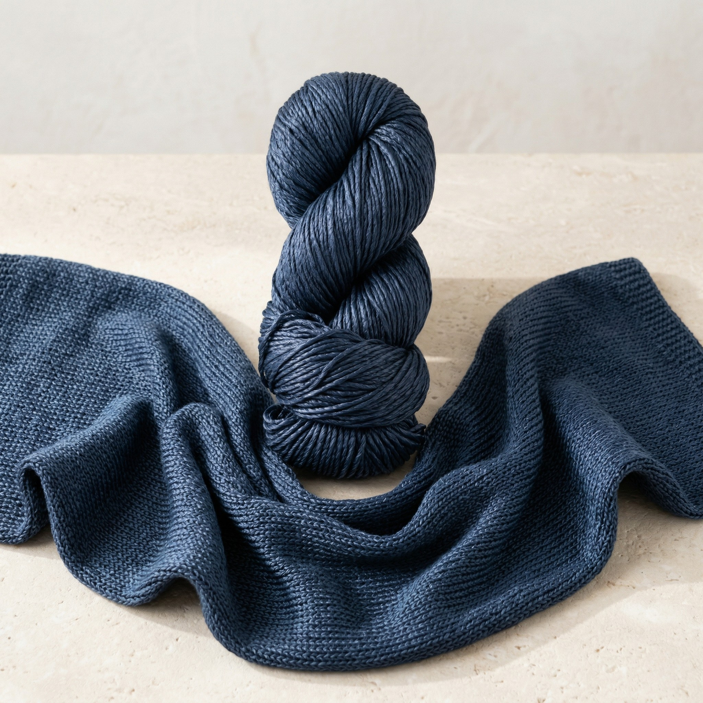 Editorial still life of Revolution Fibers Regal Mulberry Silk Yarn in Olympic Blue with softly draped knit fabric showing the yarn’s glow and fluid drape.