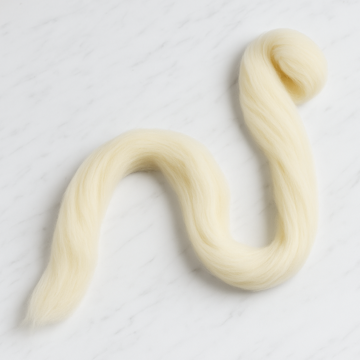 Revolution Fibers Targhee wool combed top partially unraveled strand on white marble background, continuous cream fiber ideal for spinners and dyers.
