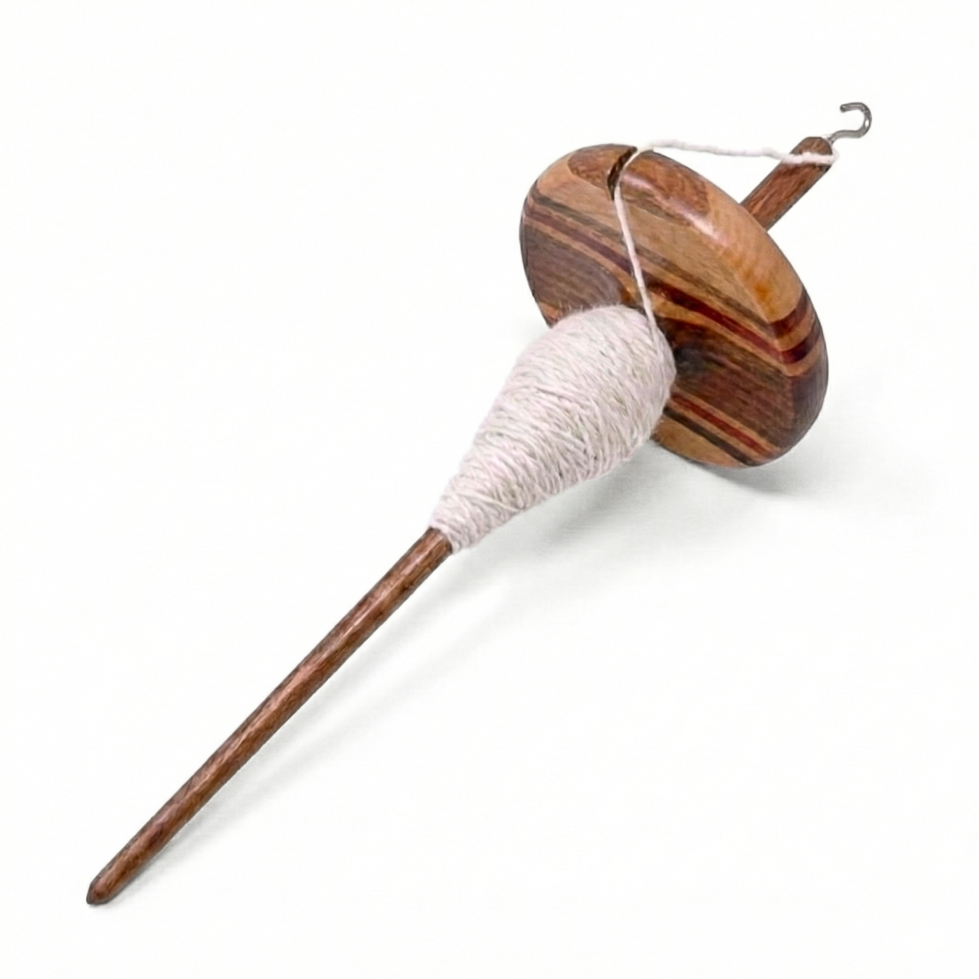 Angled laydown view of top whorl drop spindle with white singles yarn on the shaft, multi-wood wavy whorl, studio white background
