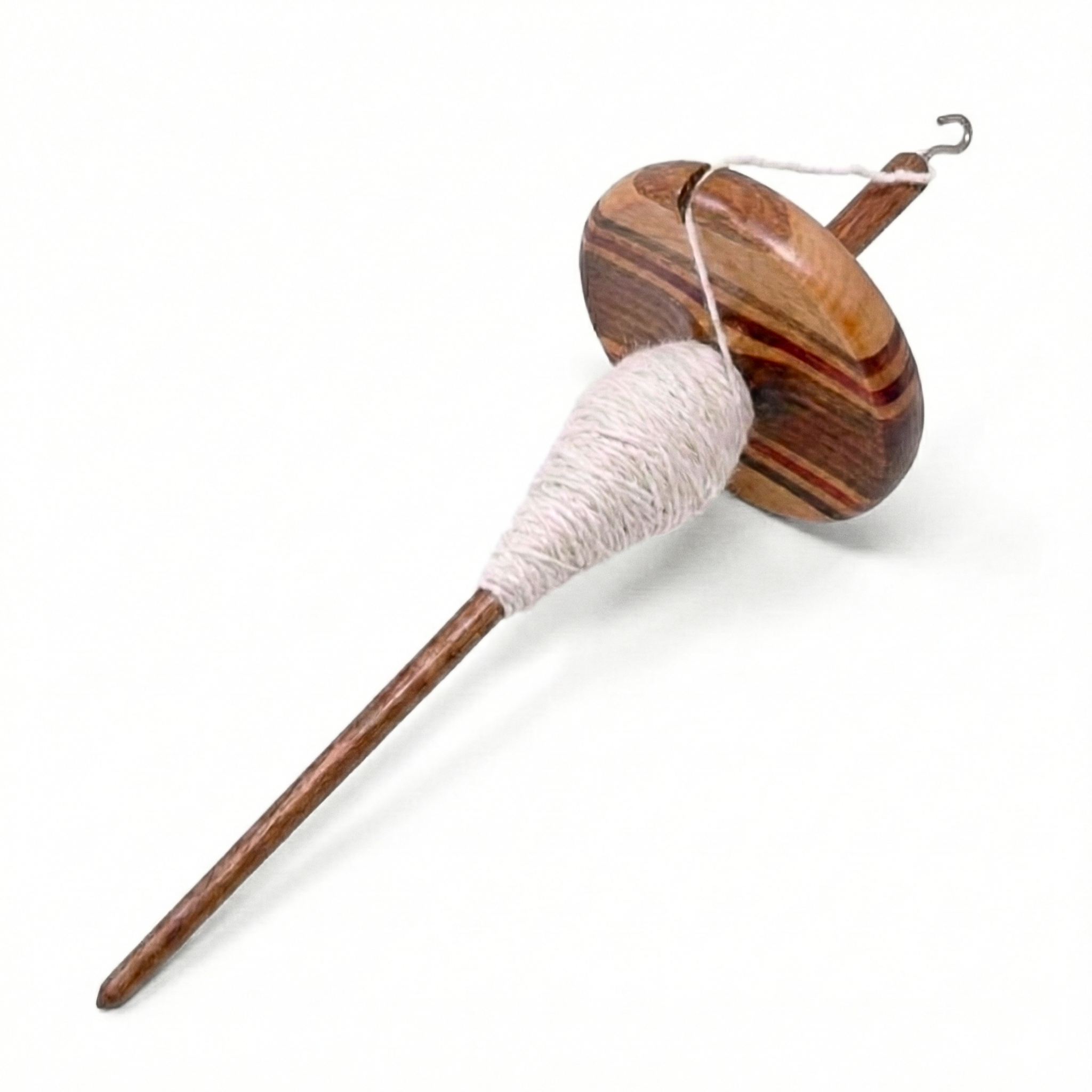 Angled laydown view of top whorl drop spindle with white singles yarn on the shaft, multi-wood wavy whorl, studio white background