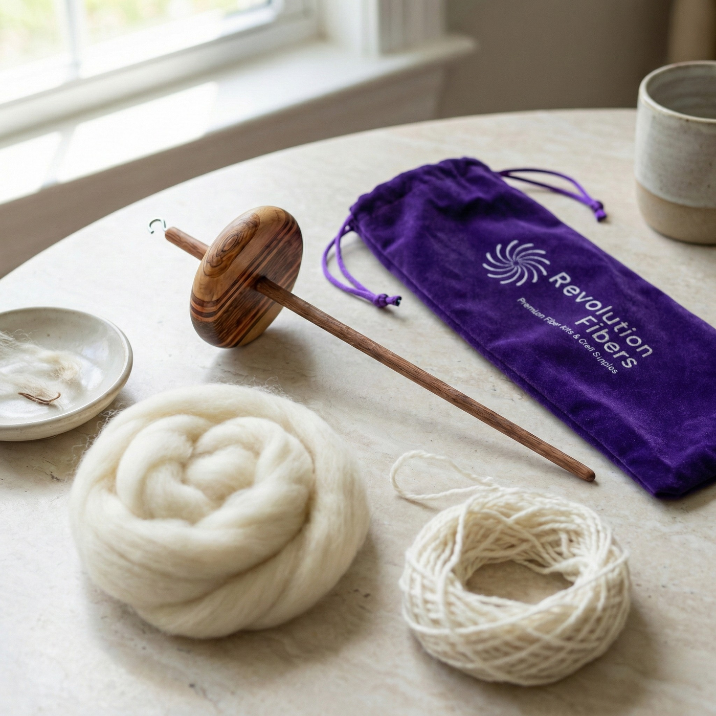 Top whorl drop spindle with purple velvet Revolution Fibers case and undyed wool roving on a bright linen surface in soft window light.