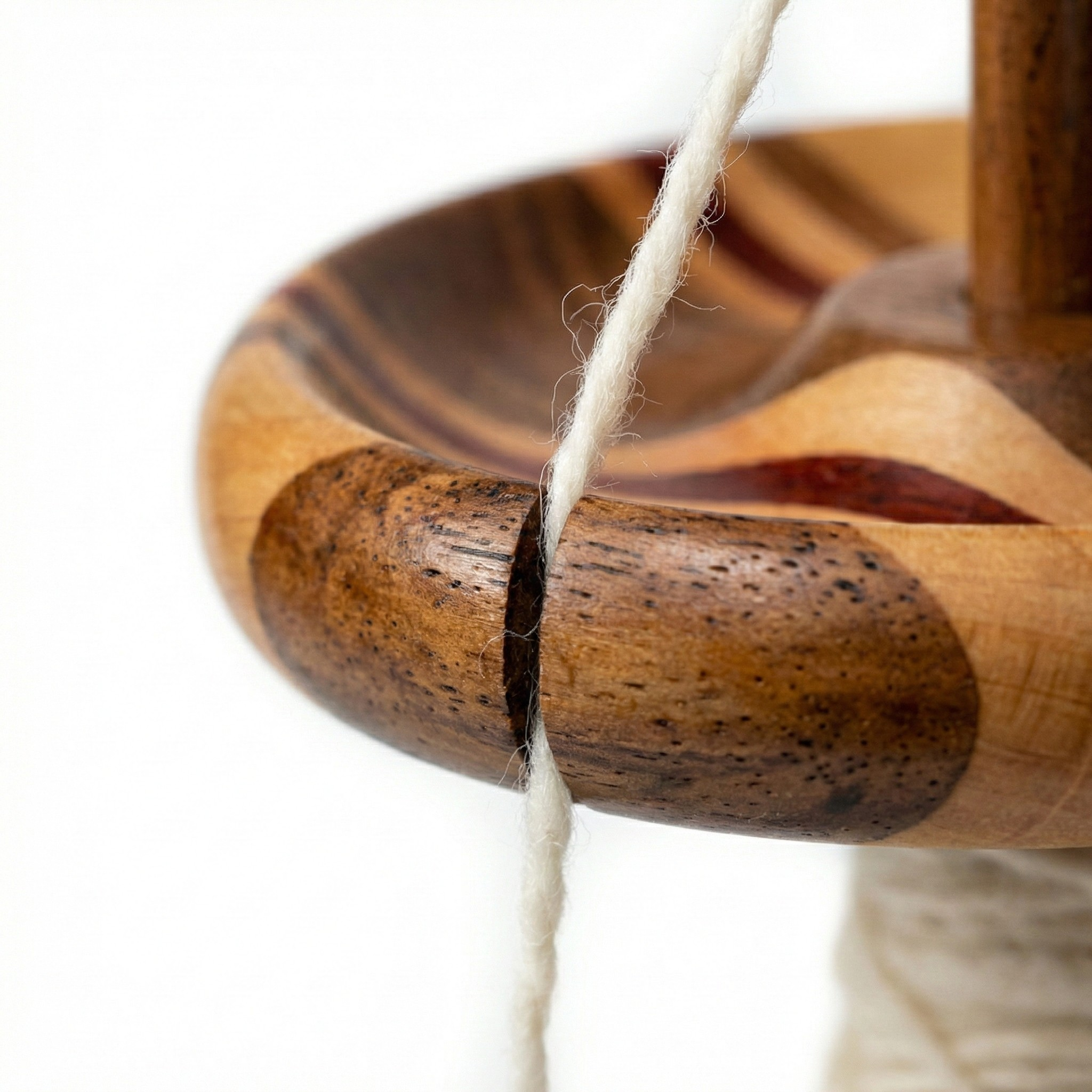 Macro close-up of the drop spindle whorl notch holding yarn in place, showing the correct yarn path during hand spinning.