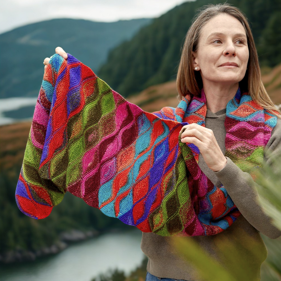 Model stretches the Hera Scarf made with Uneek 3007, revealing vibrant green-pink-blue striping across the wave pattern.