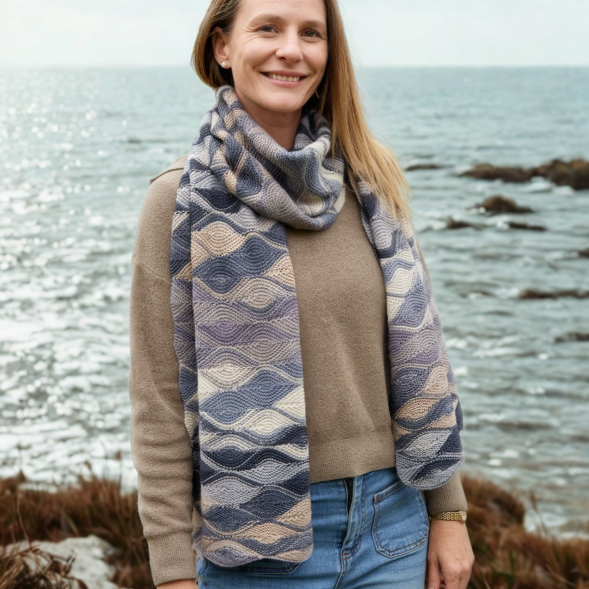 Hera Scarf in Urth Uneek 3033 draped to full length; soft lilac-grey tones stand out against an ocean backdrop.