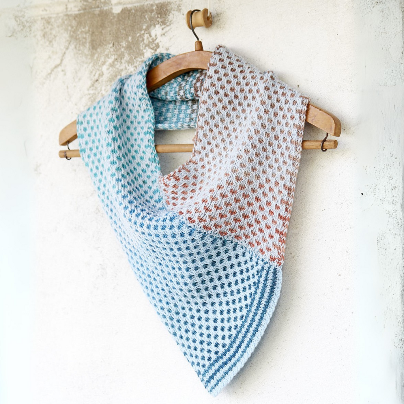 Saman Cowl knit with Urth Yarns Core 1011 and Echoes 1529, draped on a hanger to display the V-shaped front and textured, two-tone slip-stitch fabric.