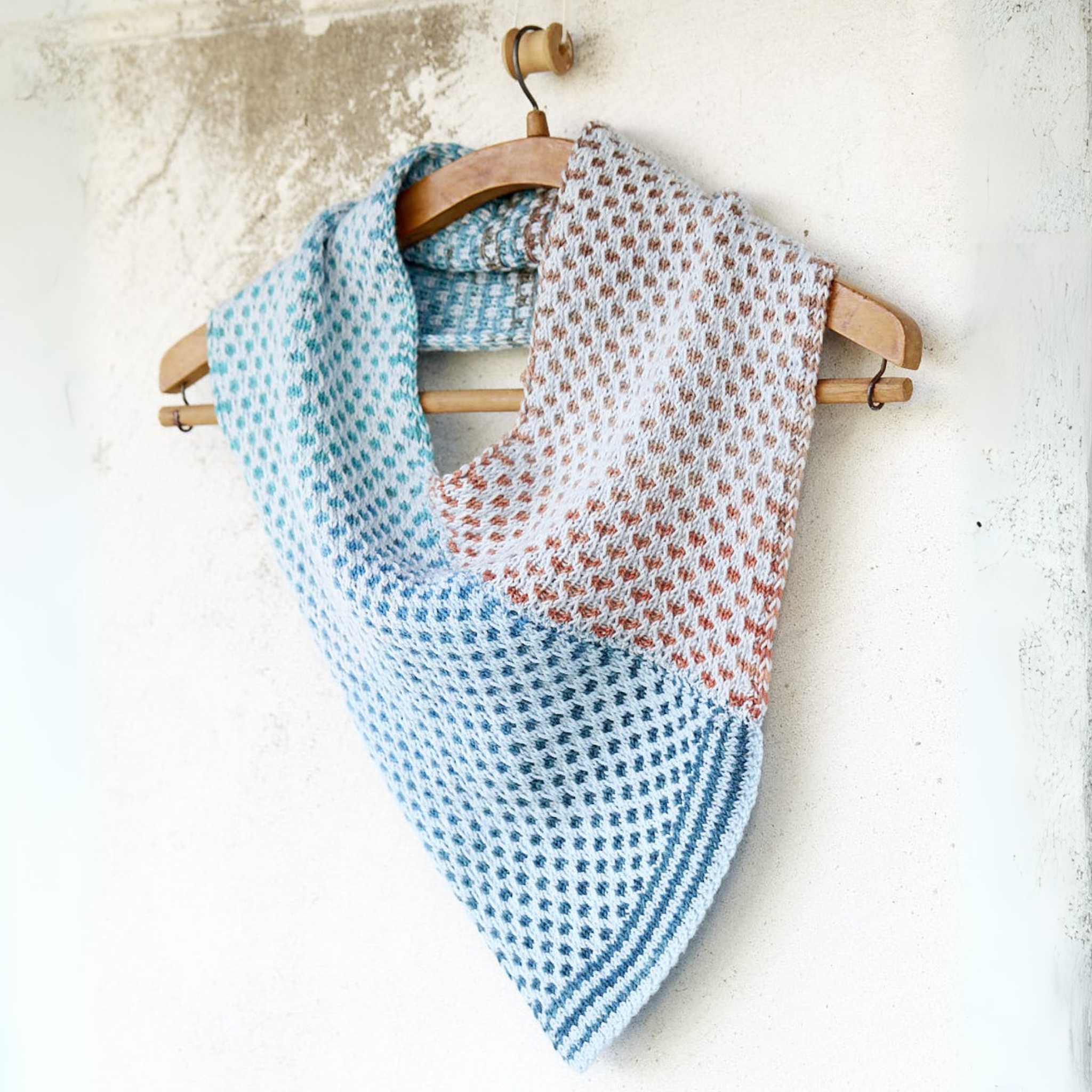 Saman Cowl knit with Urth Yarns Core 1011 and Echoes 1529, draped on a hanger to display the V-shaped front and textured, two-tone slip-stitch fabric.