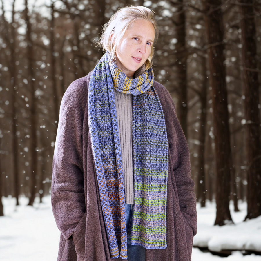 Model wearing the finished Saman Scarf knit in Urth Yarns Uneek 3001 and Harvest CPC; shows reversible slip‑stitch texture in a winter forest setting.
