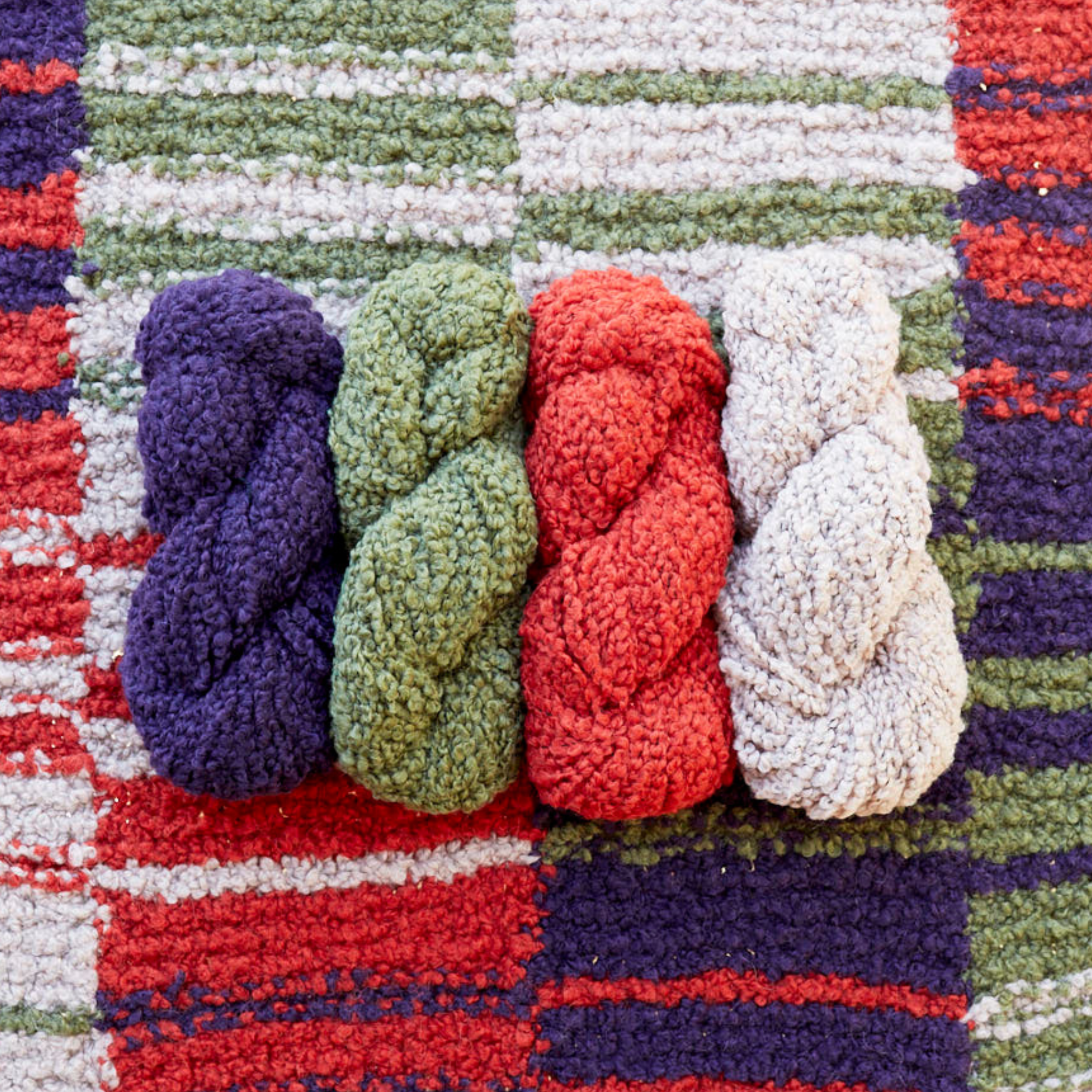 Four skeins of Lanalpaca yarn in amethyst, travertine, copper, and pumice colors neatly arranged in a row on top of the Twilight Harvest Accoloration Blanket, showcasing the matching color palette and striped design.